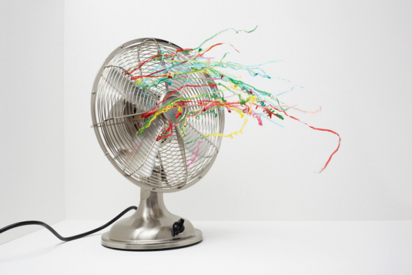 A silver metal fan with colorful ribbons blowing against a white background; concept is hot flashes